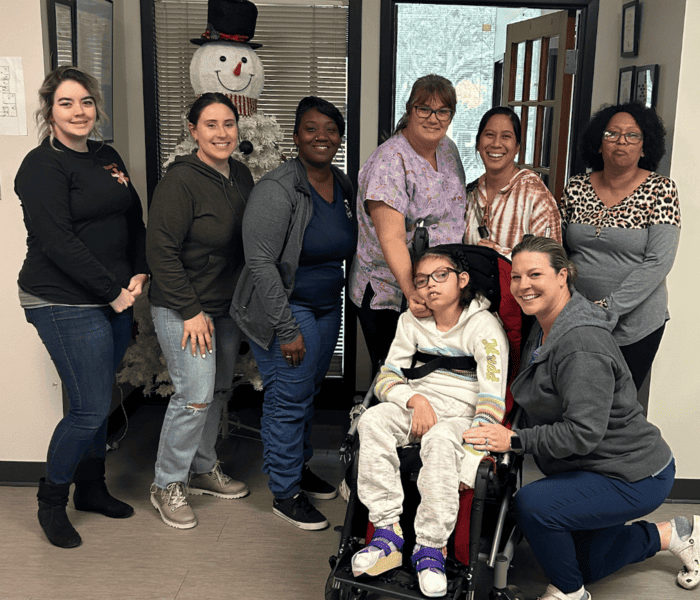 Seven women stand next to a pediatric homecare patient in a wheelchair